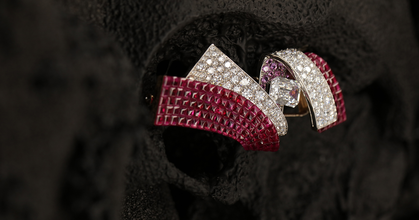 Mas Tassini studio photo, Van Cleef and Arpels haute joaillerie,DOUBLE RUBAN MYSTÉRIEUX CLIP White gold, rose gold, one DFL Type 2A emerald-cut diamond of 3.08 carats, Traditional Mystery Set buff-topped rubies, pink sapphires, diamonds.