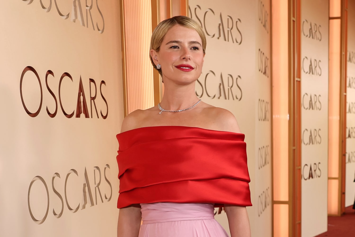JESSIE BUCKLEY, Academy Award winner, wore a CHANEL light pink bustier chiffon dress with a red satin stole. CHANEL shoes. CHANEL High & Fine Jewelry : N°5 DROP WHITE GOLD necklace in 18K white gold, diamonds, JEANNE ring in 18K white gold with diamonds, medium version, and Bouton de Camélia earrings in 18K white gold, diamonds. CHANEL Makeup, the EDGE mag